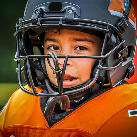 Young boy in a football uniform with a mouthguard hanging from his helmet