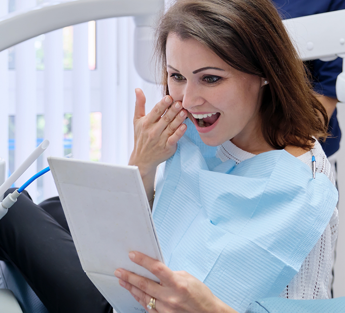 Woman looking in a mirror at her new smile after cosmetic dentistry in San Antonio