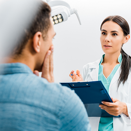 Dentist listening to a patient who is holding their cheek in pain