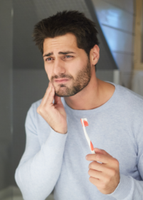 Man with a toothbrush holding his cheek in pain