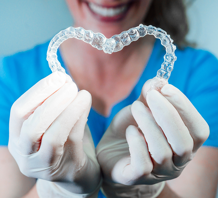 Smiling dental team member holding two Invisalign clear aligners in the shape of a heart