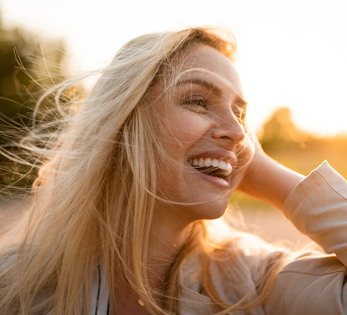 Blonde woman smiling outdoors after replacing missing teeth in San Antonio