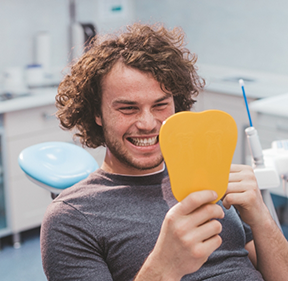 Young man looking at his smile in a mirror after receiving dental services in San Antonio