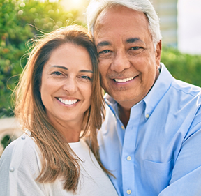 Older man and woman smiling together with green bushes in background