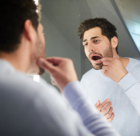 Man looking at his gums in a bathroom mirror