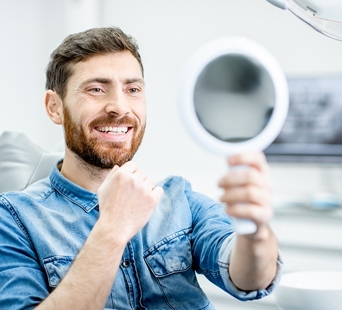 Dental patient looking at his smile in a mirror after restorative dentistry in San Antonio