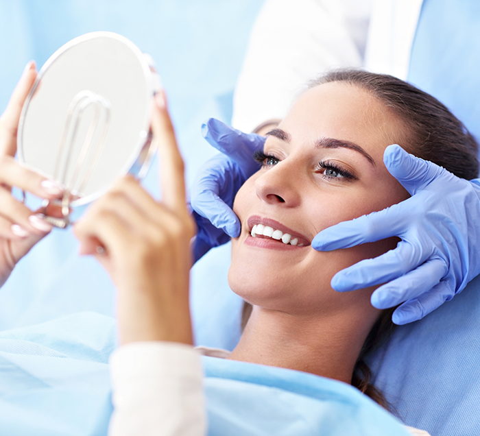 Woman in dental chair looking at her new smile in a mirror